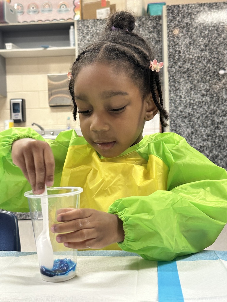 A girl uses a spoon to stir something in a cup.