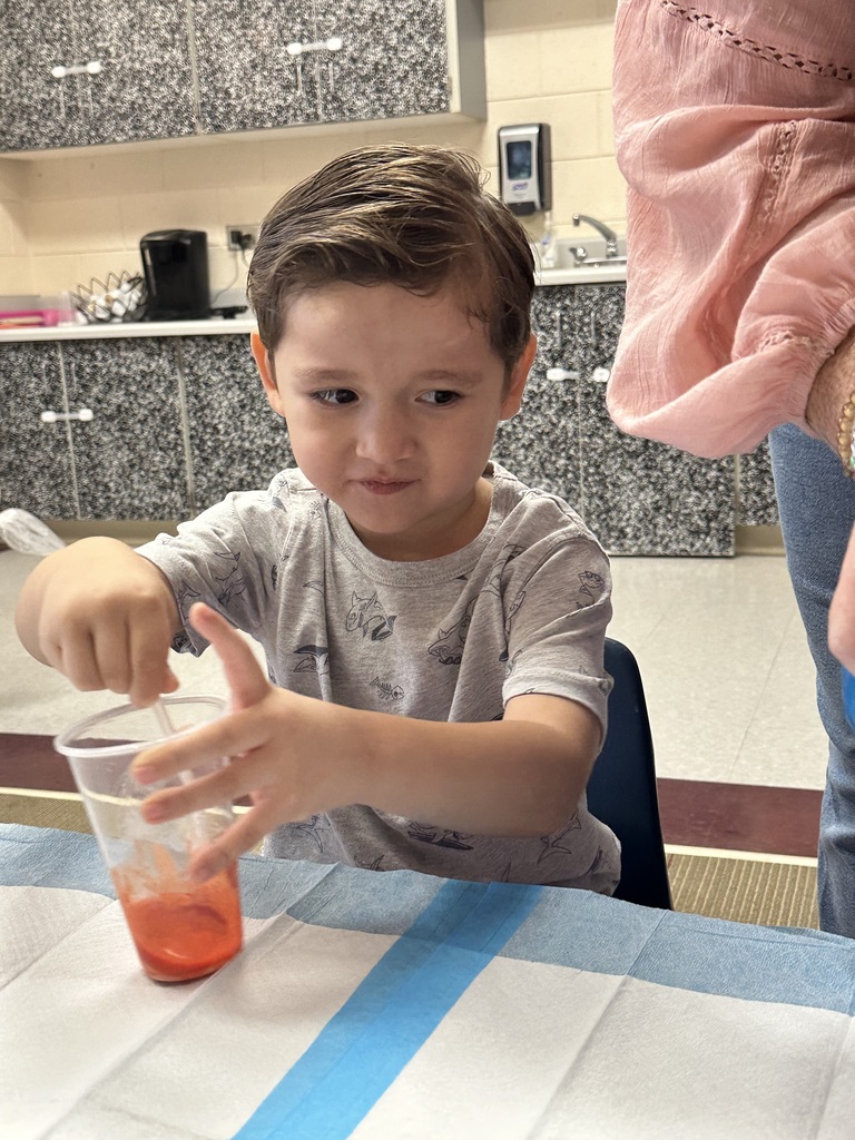A boy uses a spoon to stir something in a cup.