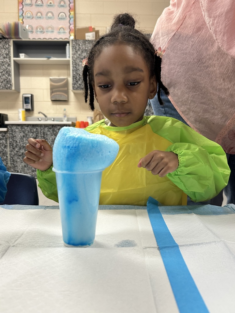 A girl with an excited expression watches foam rising from a cup.