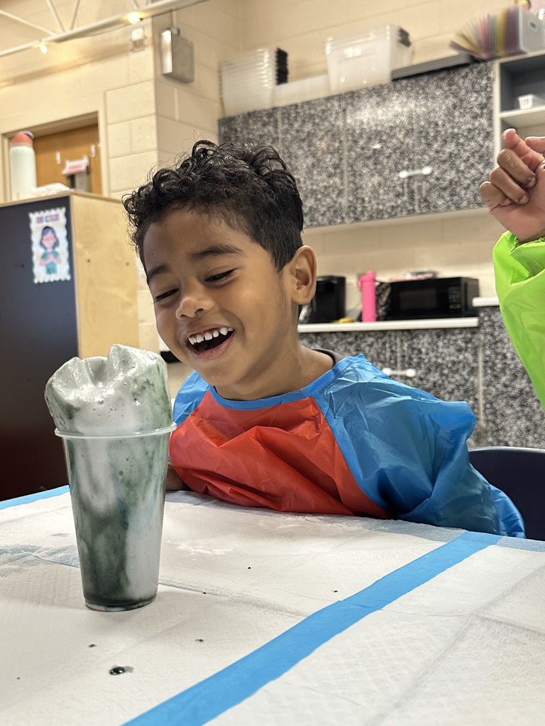 A boy with an excited expression watches foam rising from a cup.