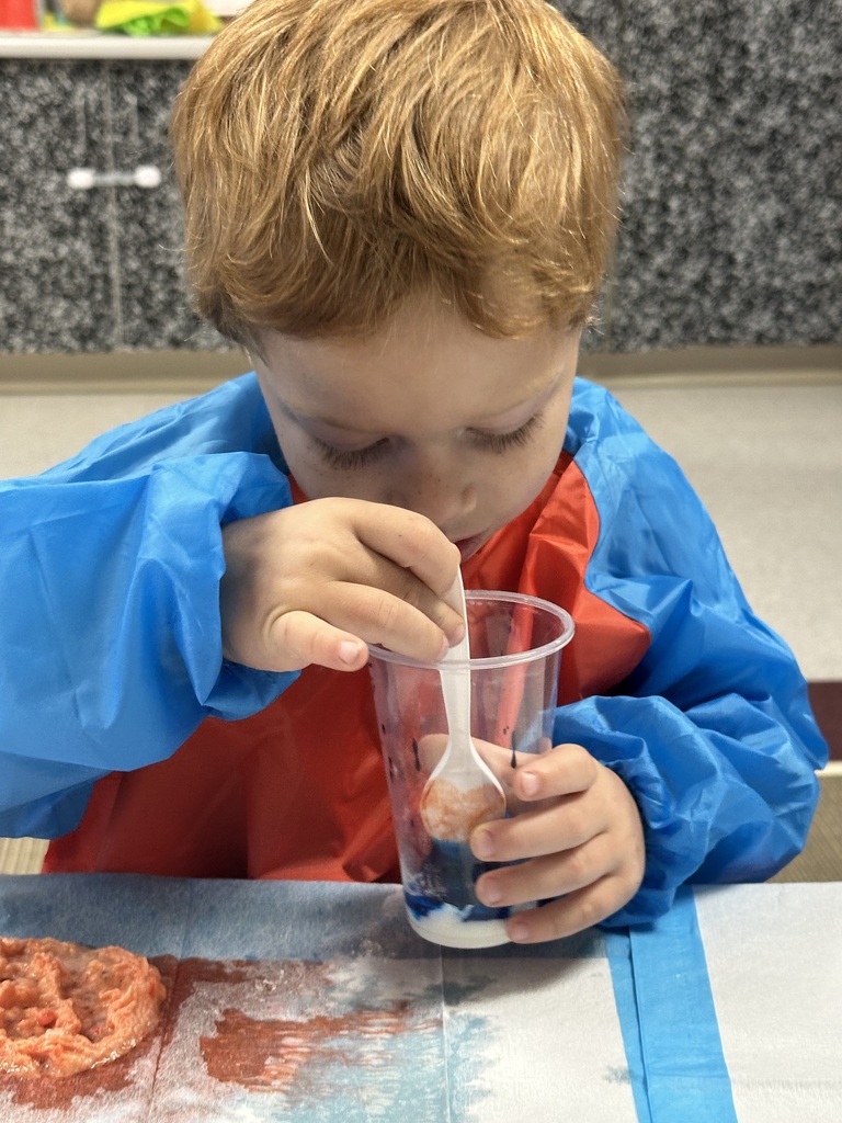 A boy uses a spoon to stir something in a cup.