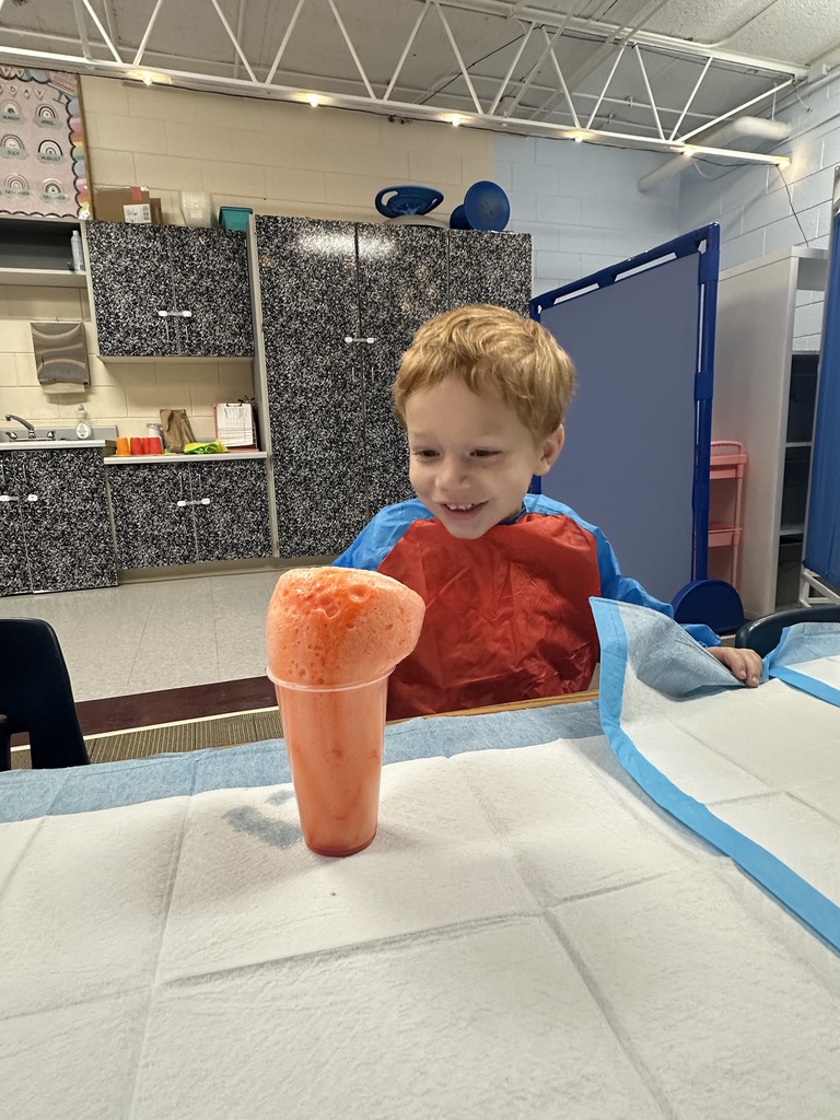 A boy with an excited expression watches foam rising from a cup.