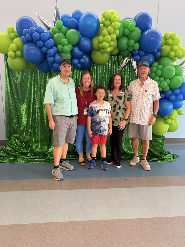 4 adults and a young child standing in front of balloon arch and smiling at the camera