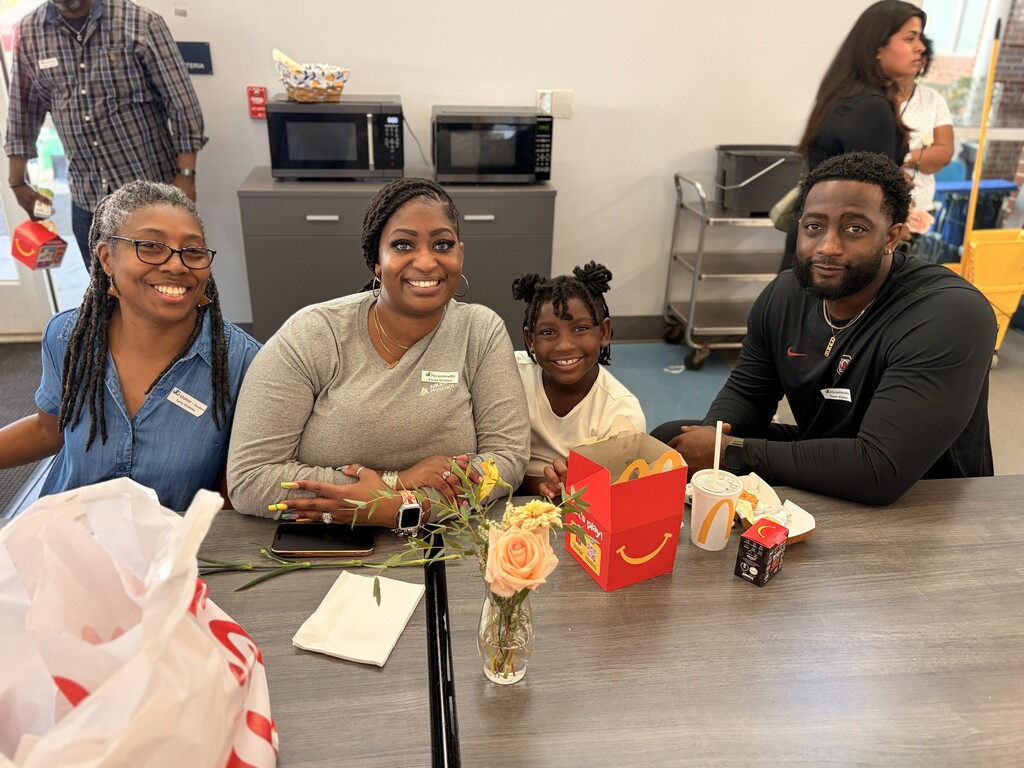 A family sits at a table with a McDonald's box, flowers, and napkins. Other people are in the background.