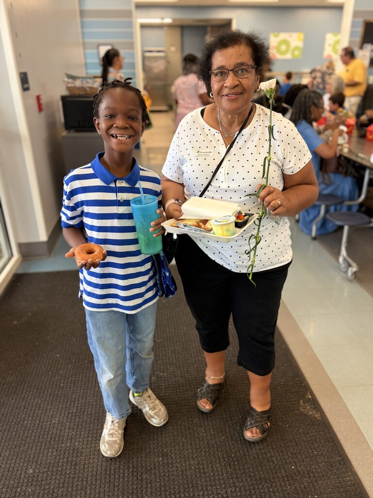 A woman with glasses and a flower in her hair stands with a boy in a striped shirt.