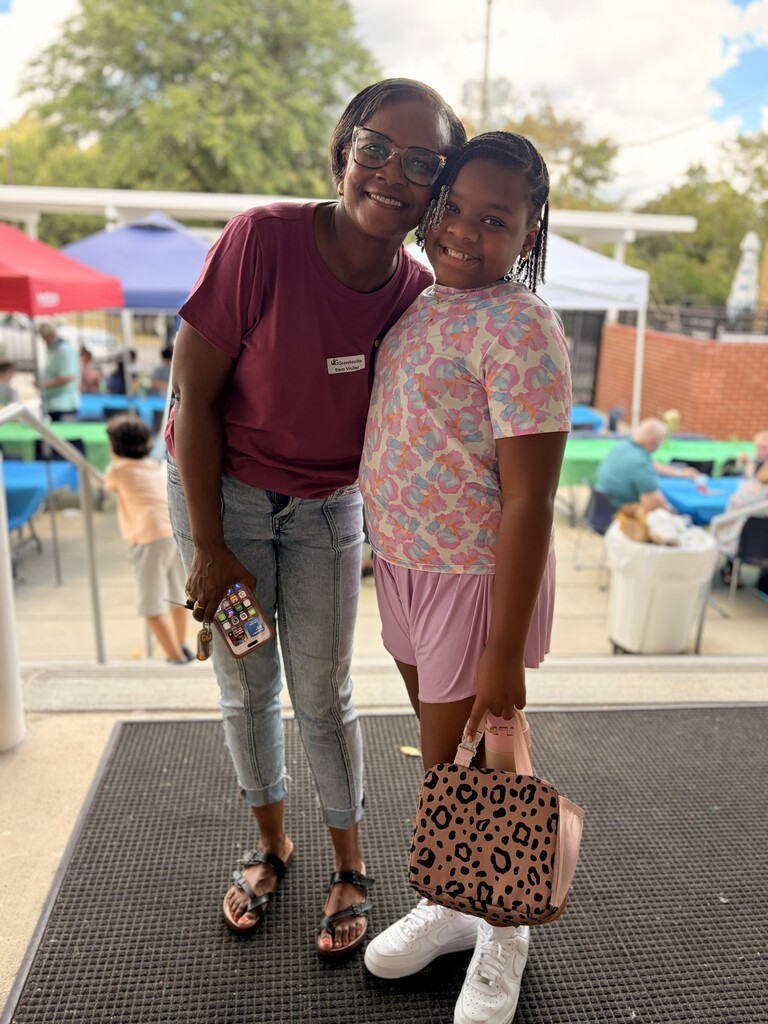 Two women smiling. One wearing glasses and a maroon top. Other holding a leopard print bag.