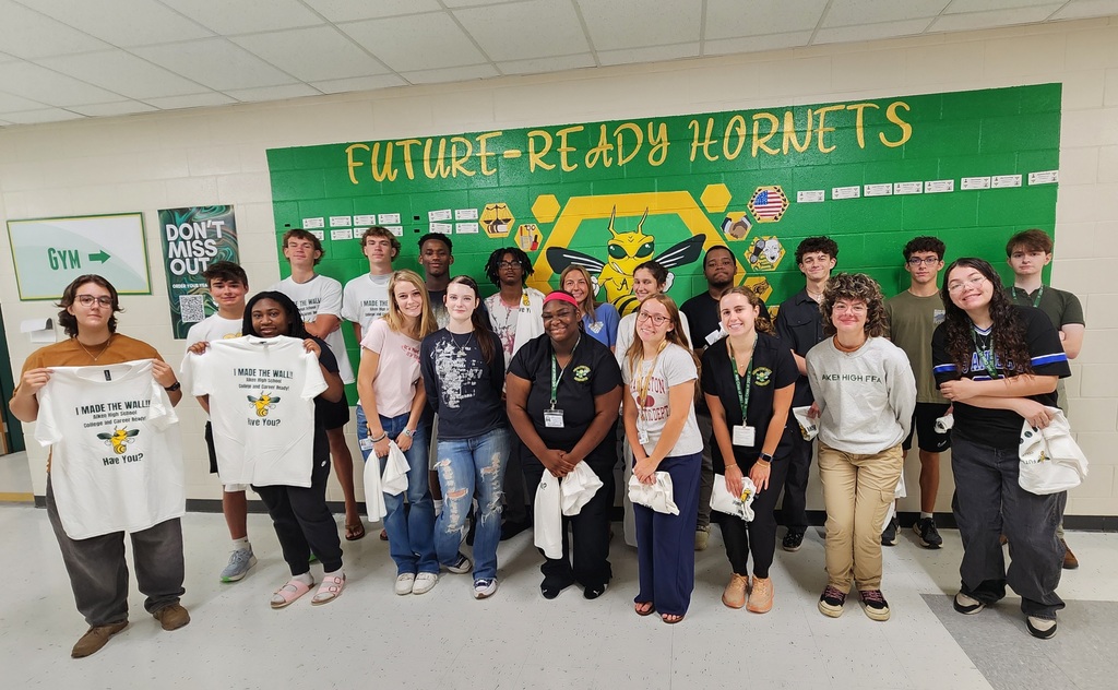 A group of students standing in front of a green wall.
