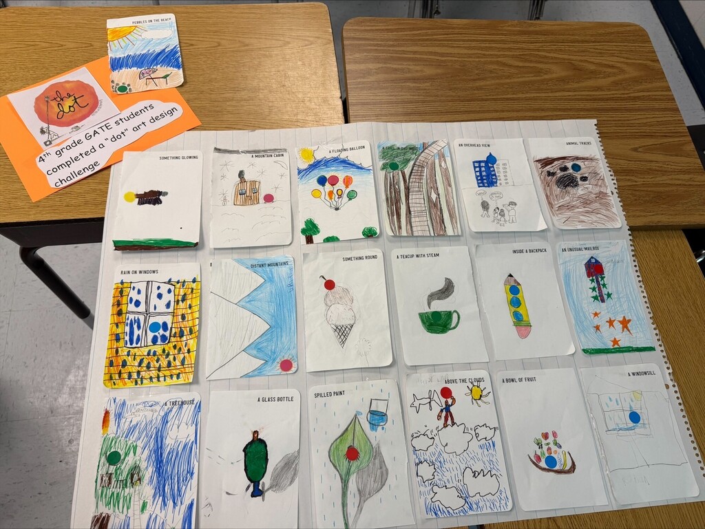 Display of student artwork on a white backdrop, arranged in rows on a classroom desk. Each drawing is on a separate small card.