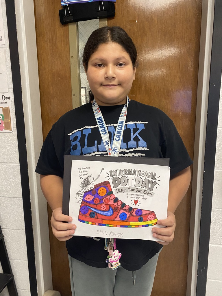 A young person holds a shoe drawing. They wear a black T-shirt with the word "Blik" and a lanyard. They stand in front of a closed door.