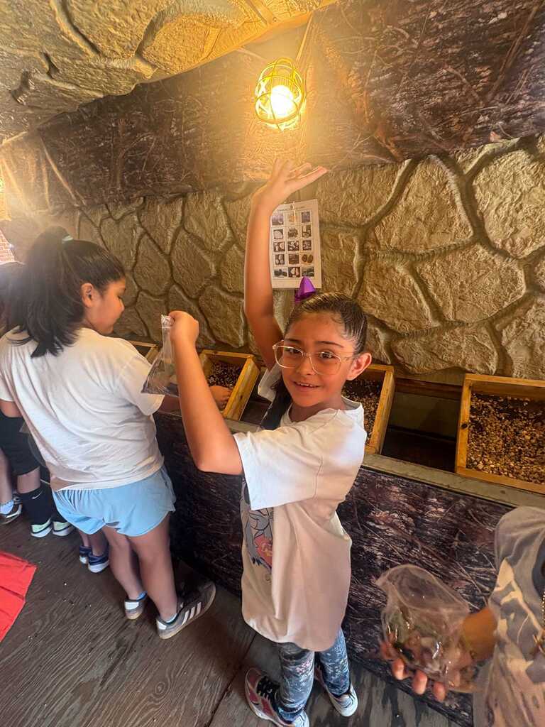 Children in a room with stone walls, examining items in their hands, one raising hand.