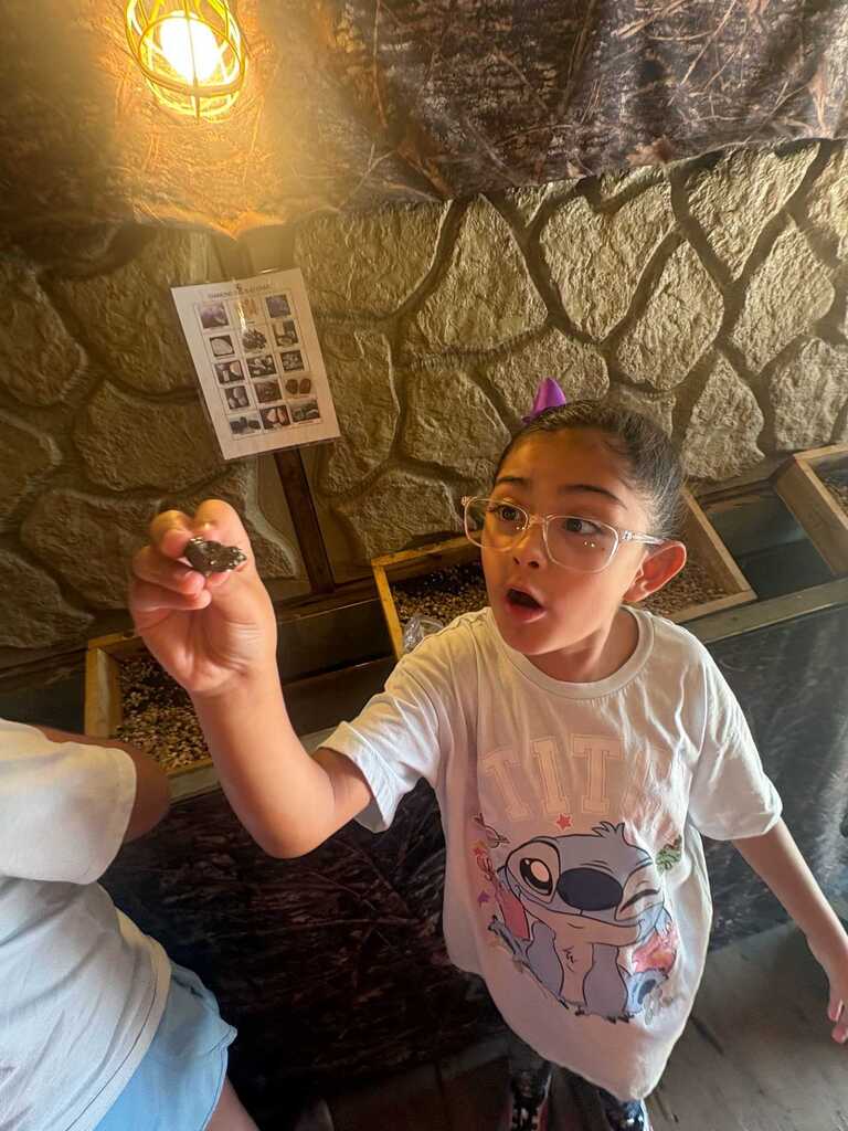A child wearing glasses holds a small object, standing in a room with a stone wall and a light.