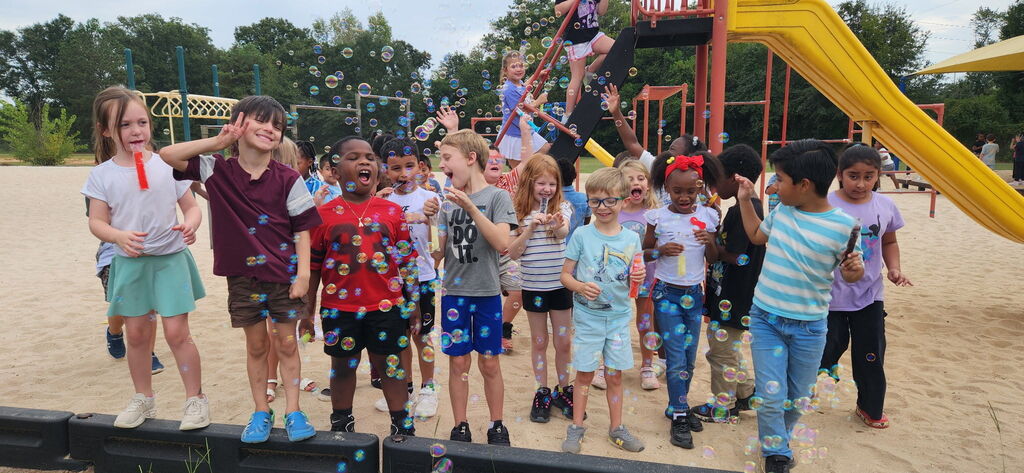 Group of children in casual clothing play in a playground with a yellow slide.
