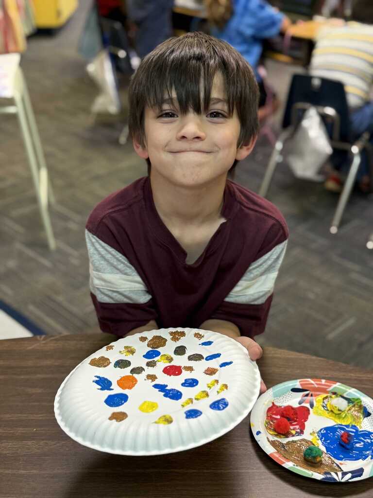 A young boy displays two plates, one with multicolored dots and the other with a colorful mess.