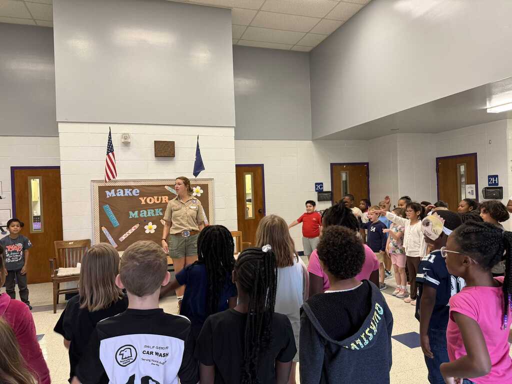A group of students listens to a woman standing in front of a bulletin board.