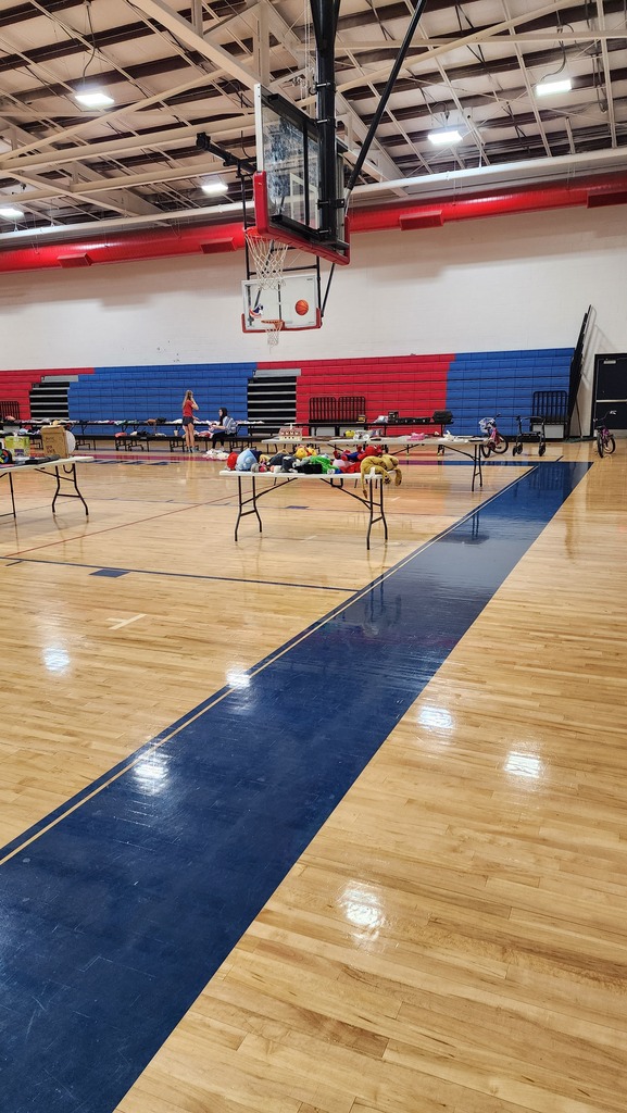 An empty basketball court with blue and white walls, wooden floors, and two tables in the middle.