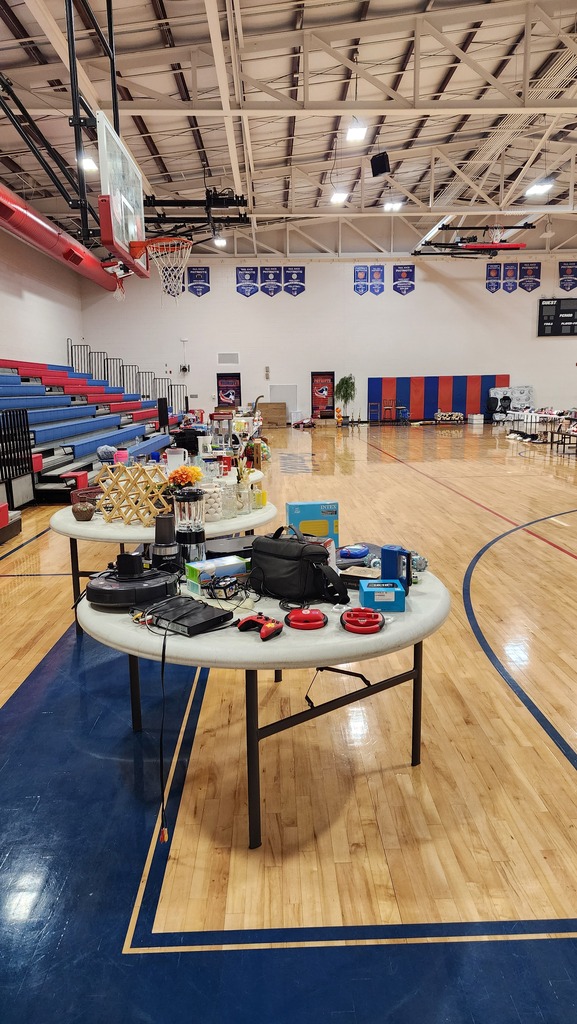 An indoor basketball court with two tables full of items. The court has blue and wooden floors.