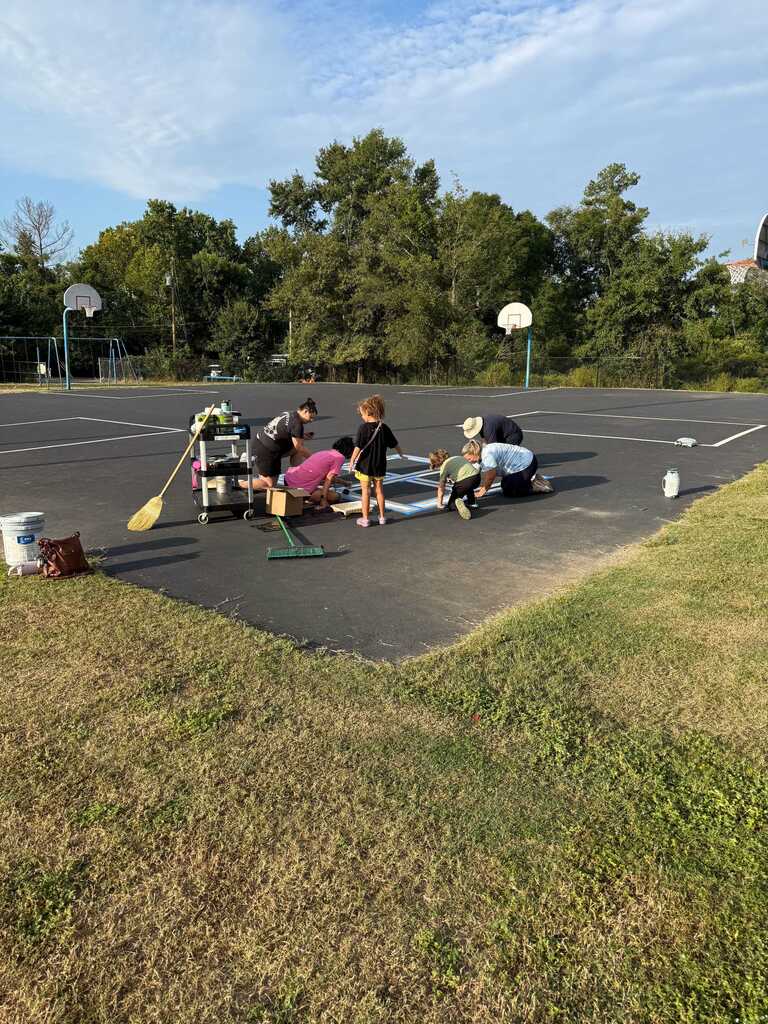 Five people work on a basketball court. One holds a paddle, another a broom, and a third wears a hat. A bucket and bottle sit nearby.