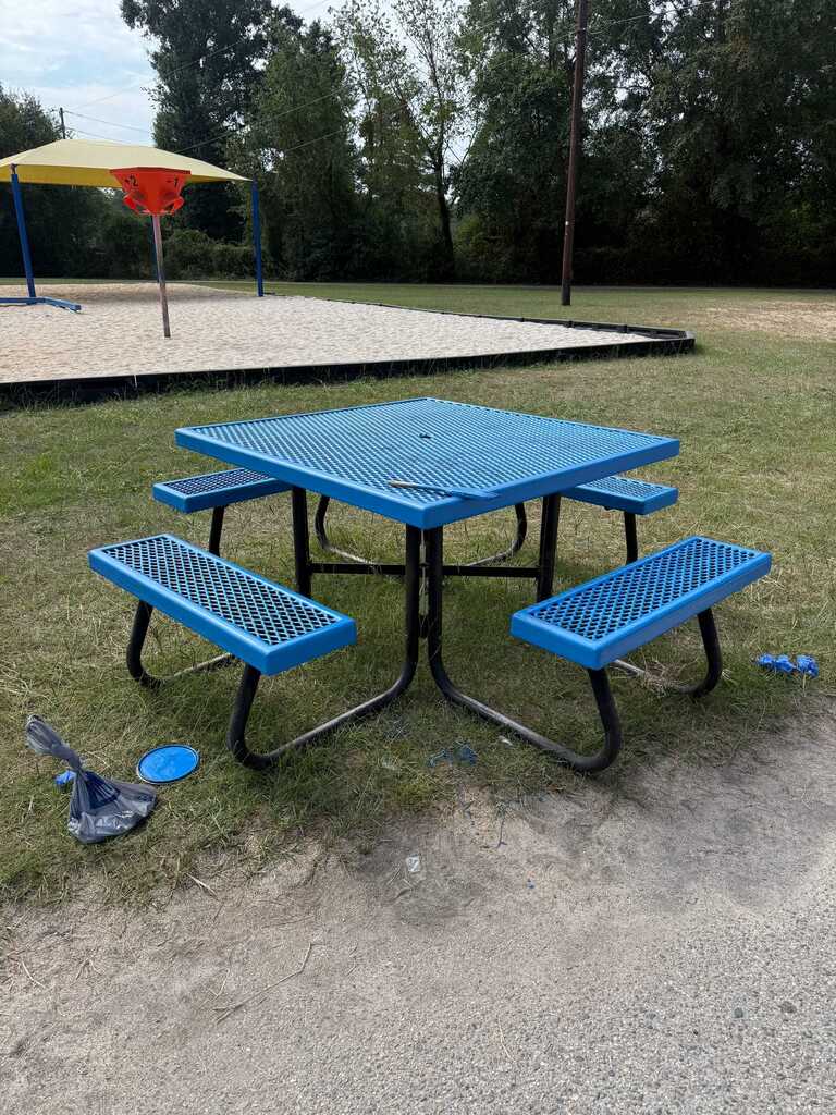 A blue picnic table with benches in a park. A frisbee lies on the ground nearby.