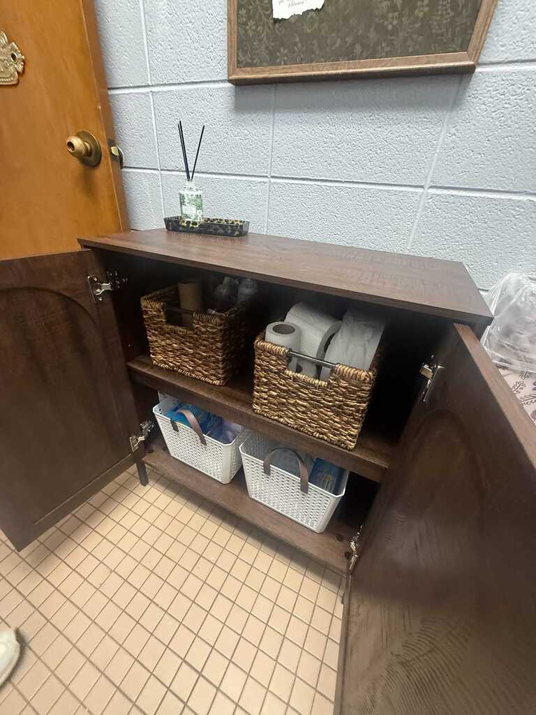 A bathroom with wooden cabinets open to reveal shelves. Three baskets sit on the shelves. A framed picture hangs on the wall above.