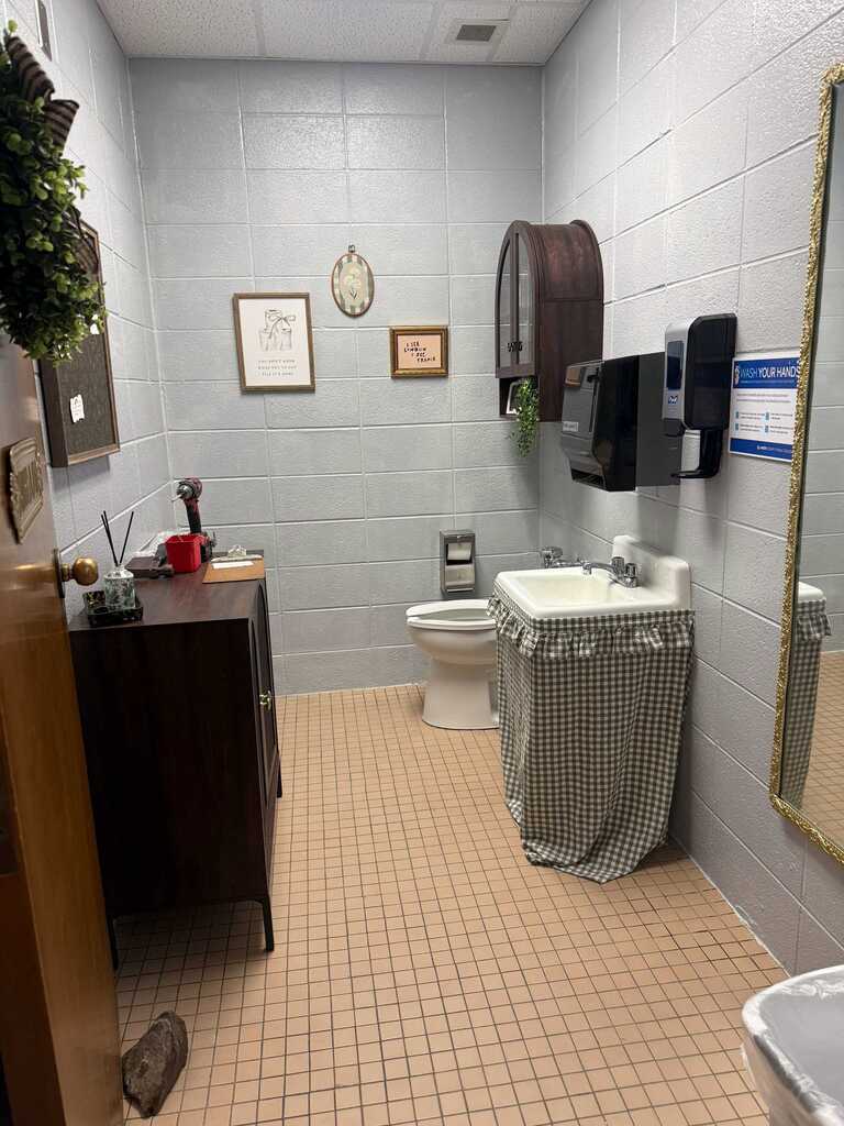 A bathroom with tiled flooring, a sink, mirror, toilet, a wooden cabinet, and two framed pictures on the wall.