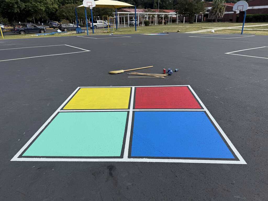 An empty paved court with a square in colorful blocks. There are objects on the ground in the center.