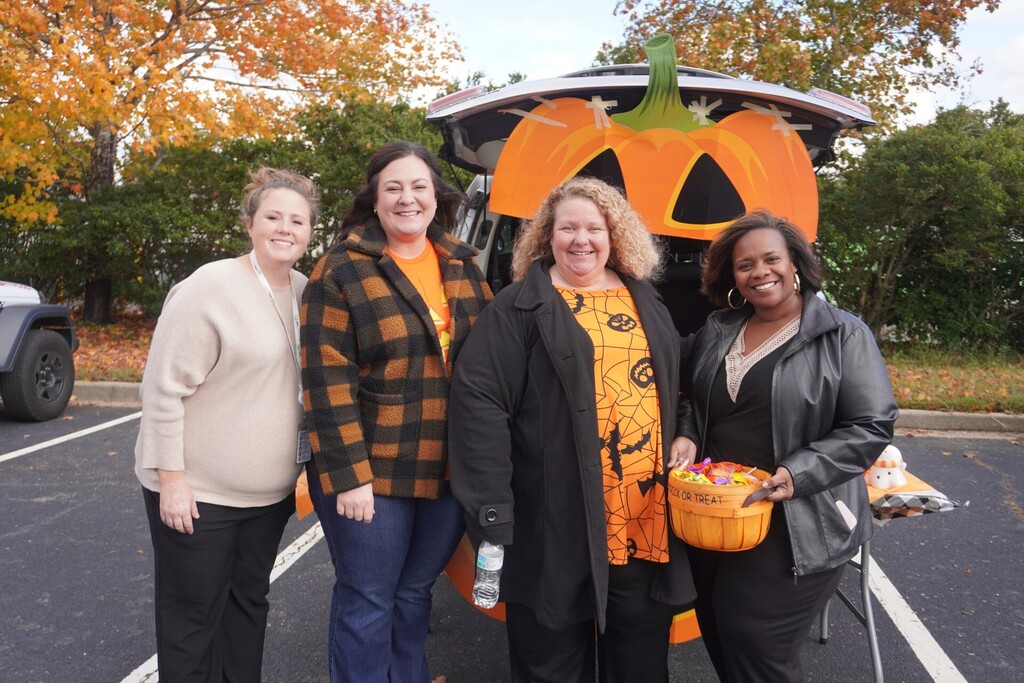 HR employees smiling in front of trunk of car decorated with pumpkin decor for trunk or treat event.