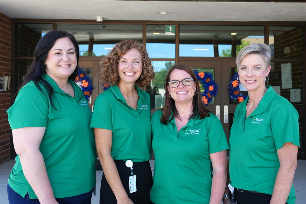 Group of four HR associates smiling in front of Midland Valley High School.