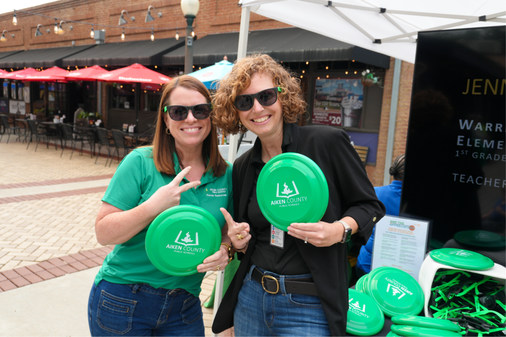 Two HR associates smiling together at Amp the Appreciation while holding ACPSD frisbees.
