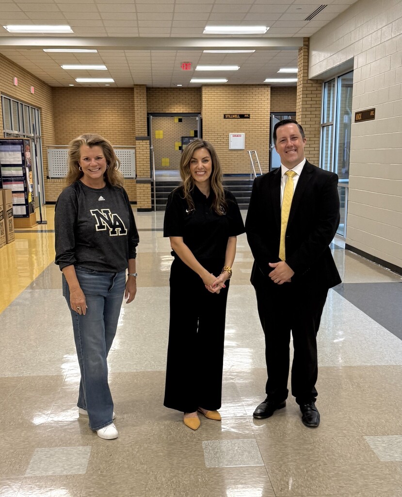 Three people in business attire stand together in a hallway. Two women and one man.
