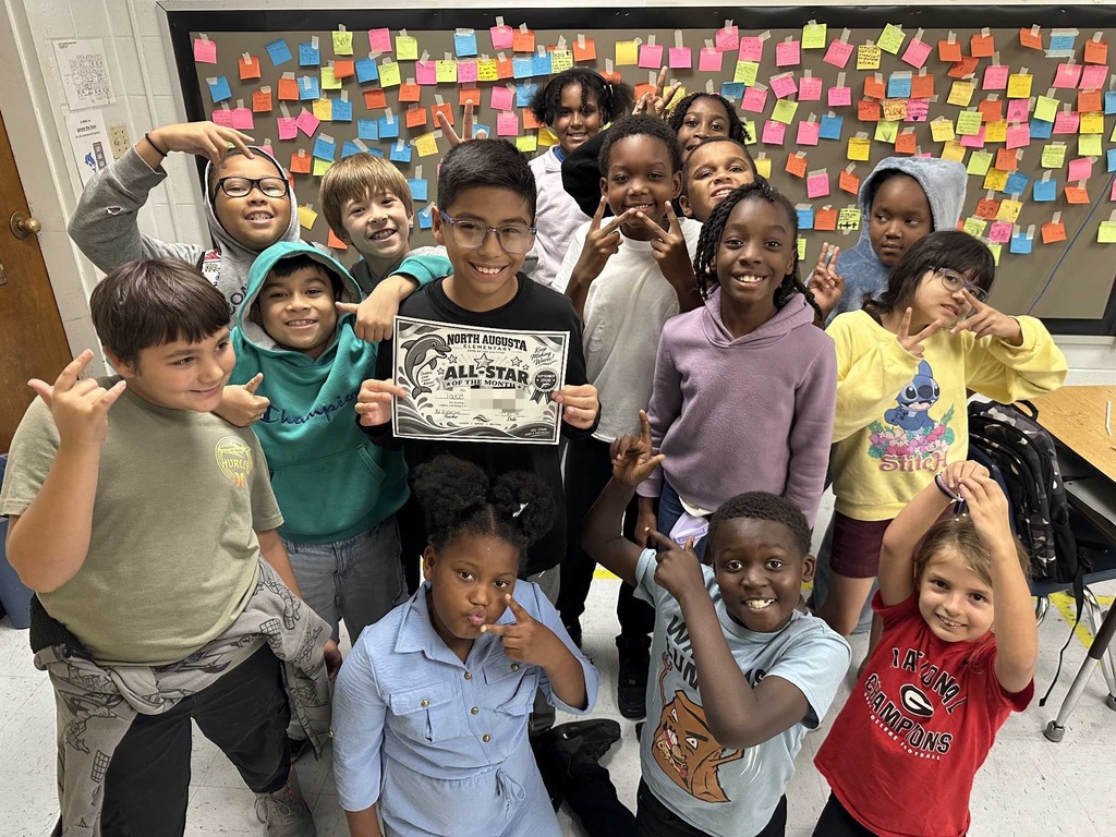 A group of students in a classroom with a bulletin board covered in colorful sticky notes.
