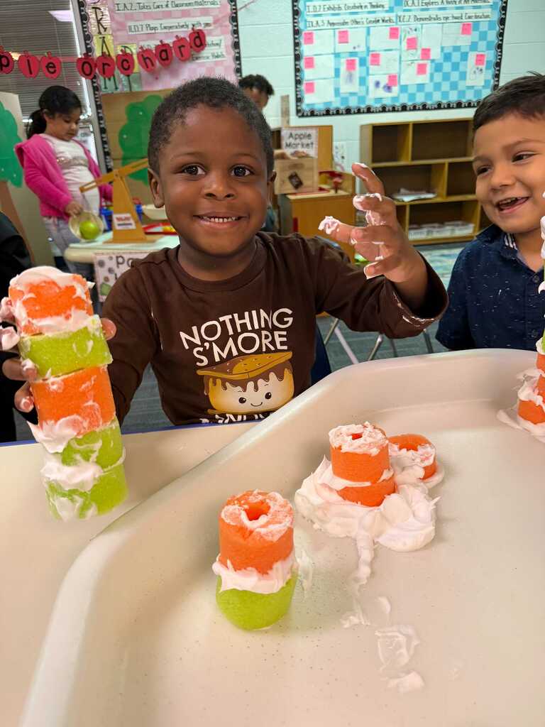 Two children holding orange and green items, possibly for an activity. One holds a stack, the other has items on a tray.