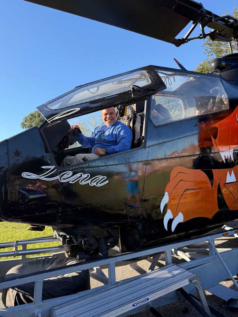 A helicopter with the name Lena on its side, parked on a trailer. A person sits in the pilot's seat.