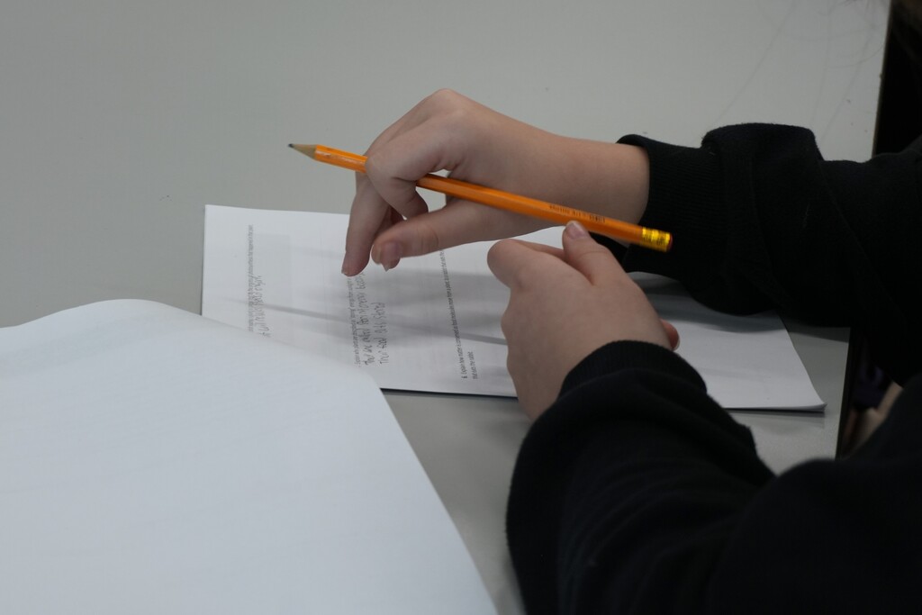 Person with pencil over white paper, writing on lined paper with one hand on a table.