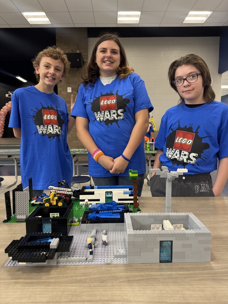 Three young people in blue T-shirts with the word "WARS" stand behind a table with Lego creations.