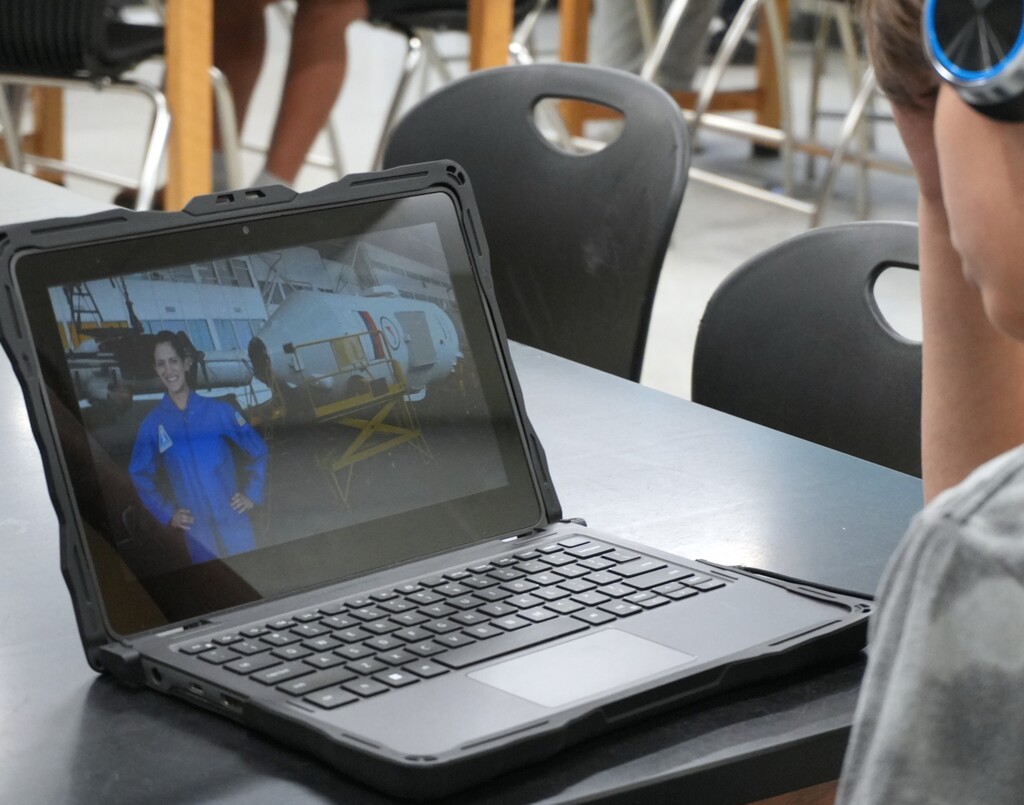 Person watching a video on a laptop screen showing a woman in a blue jumpsuit.