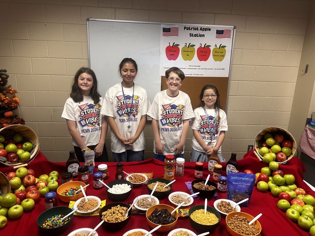 Students standing behind a table that is filled with toppings