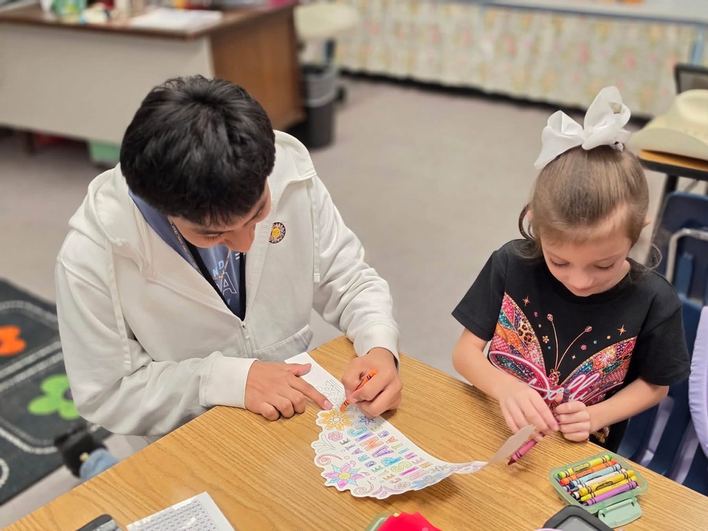 An adult and a child work on a craft project together at a table in a classroom.
