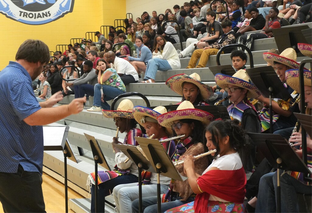 A man directs a band of students wearing sombreros and playing instruments in a gymnasium.