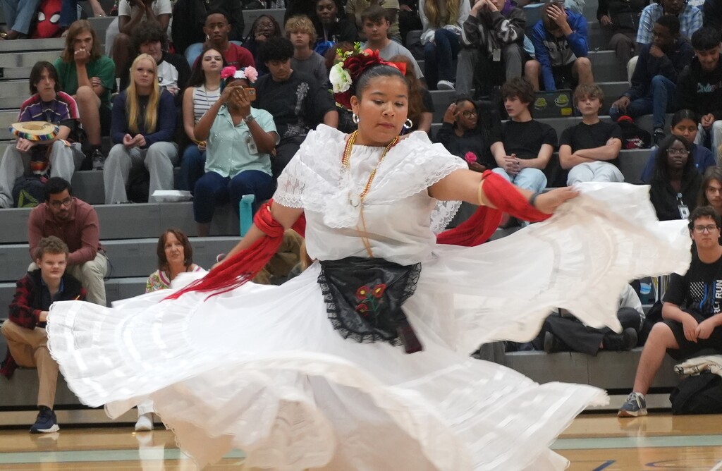 A woman in a white dress and red accessories dances on a basketball court, surrounded by an audience.