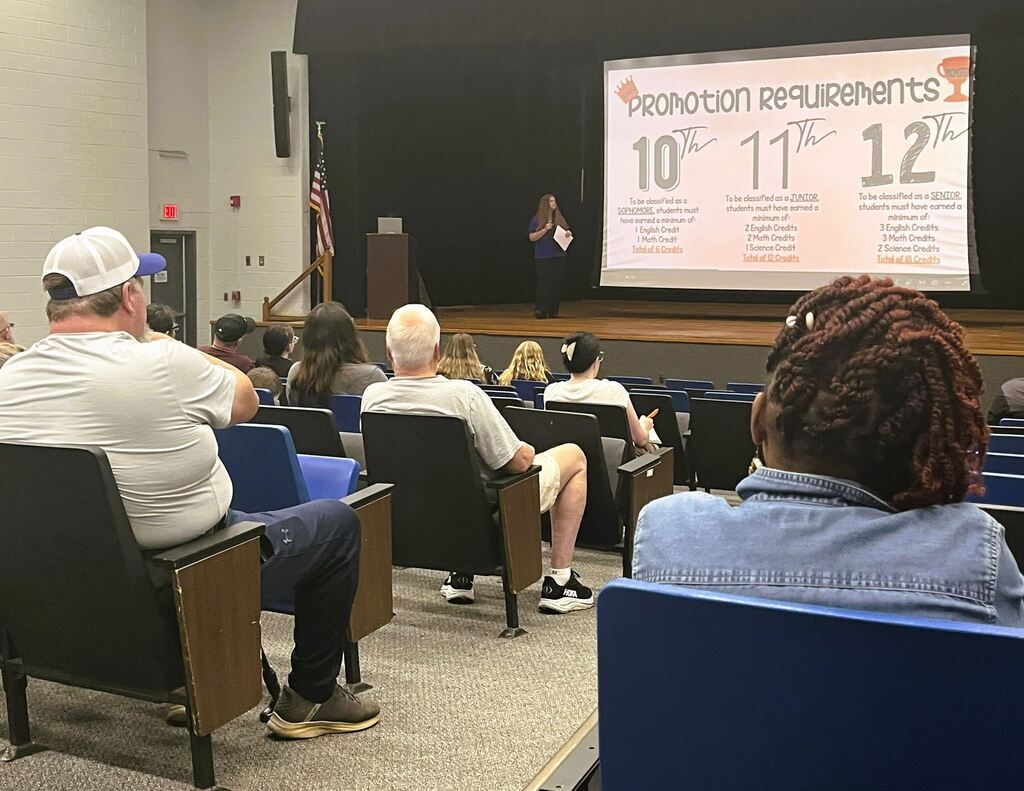 Parents sitting in auditorium in front of a screen with counselor speaking to them