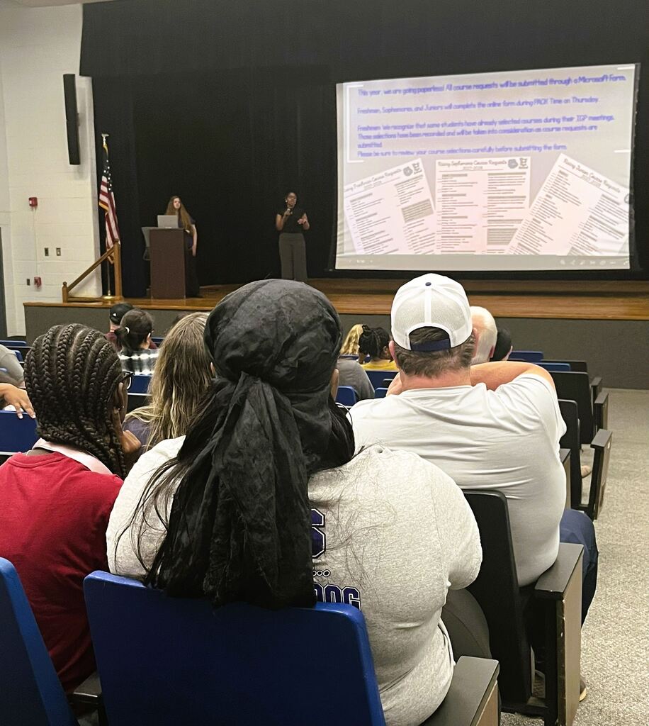 Parents sitting in auditorium in front of a screen with counselor speaking to them