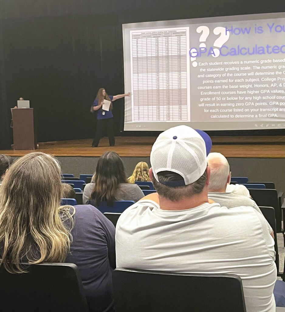 Parents sitting in auditorium in front of a screen with counselor speaking to them