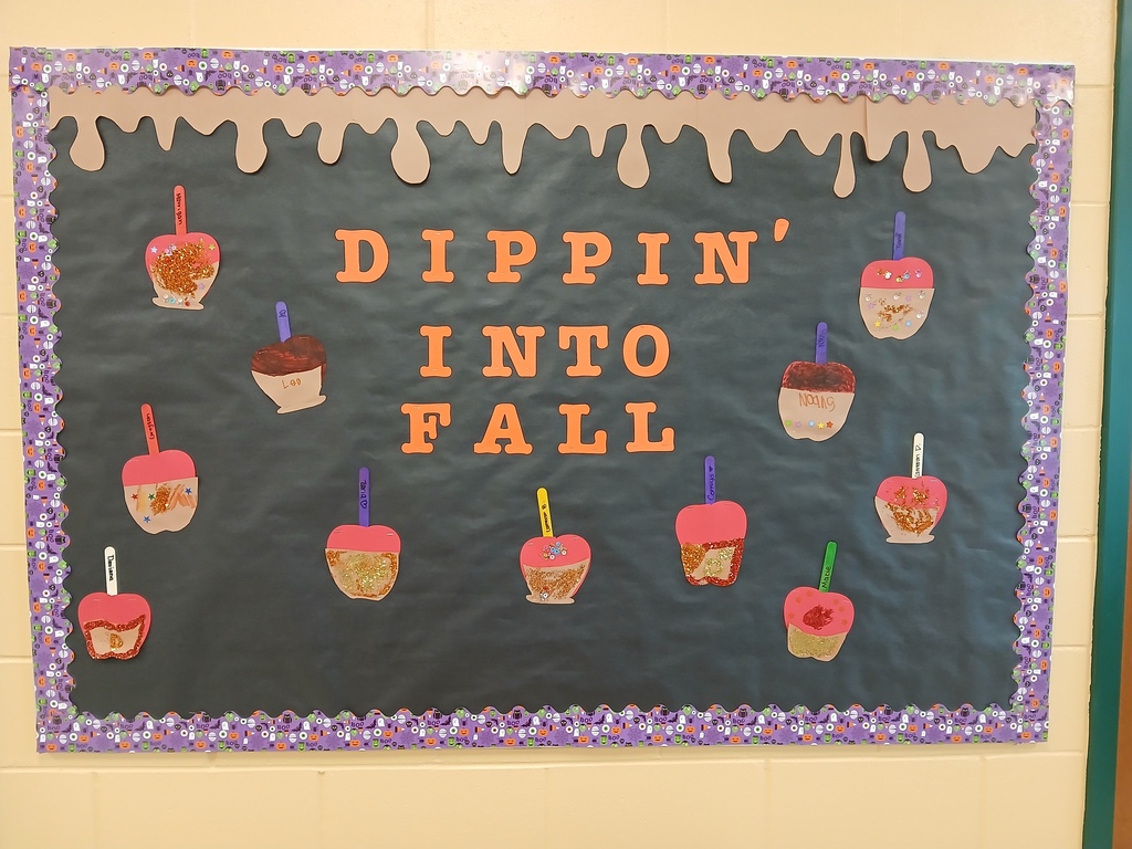 Black bulletin board with the words "Dippin' Into Fall" and some candied apples scattered around it.