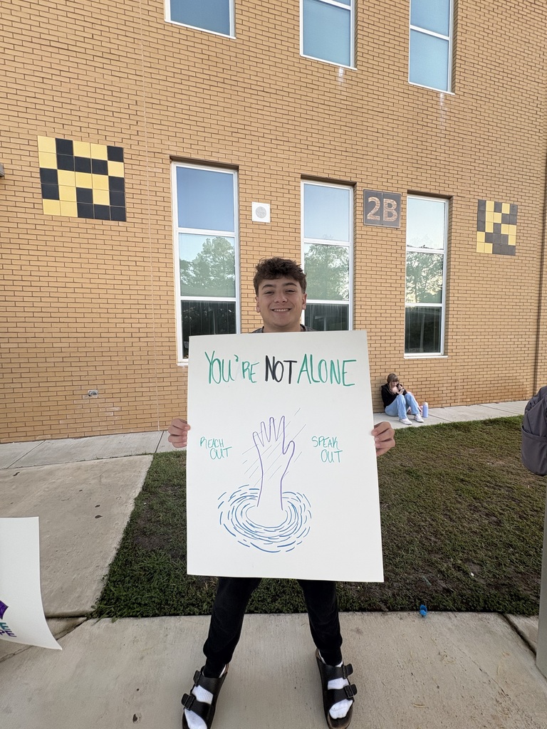 Boy standing in front of school with a You're Not Alone hand drawn sign. 
