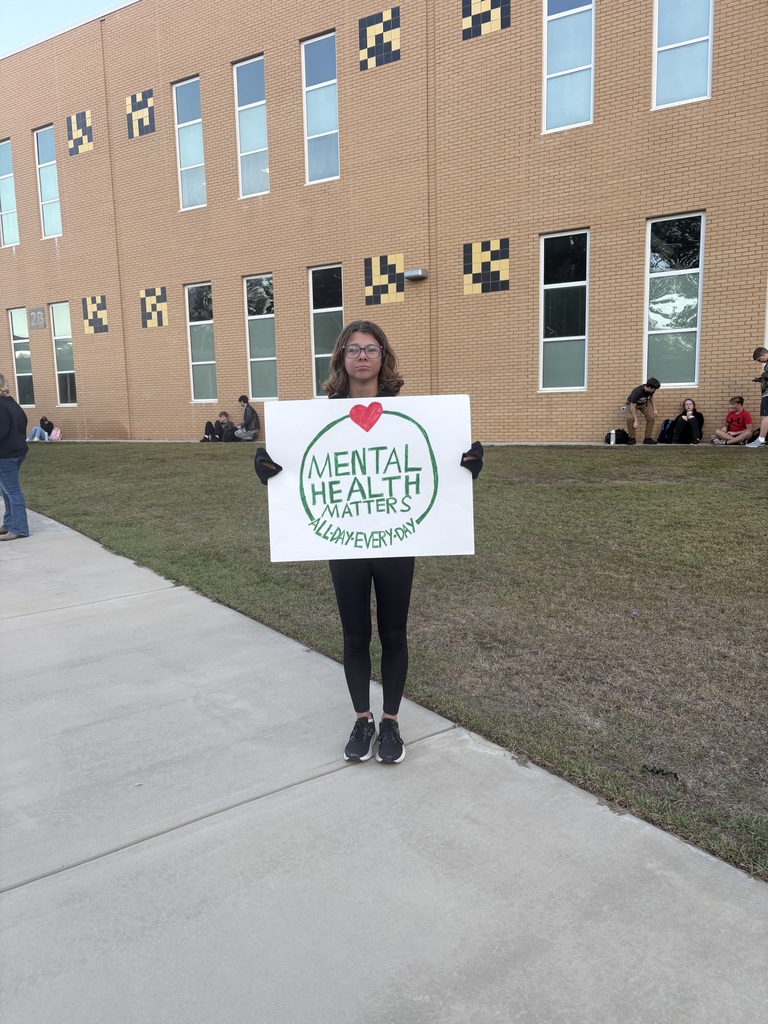 Student standing in front of school with sign that states Mental Health Matters."