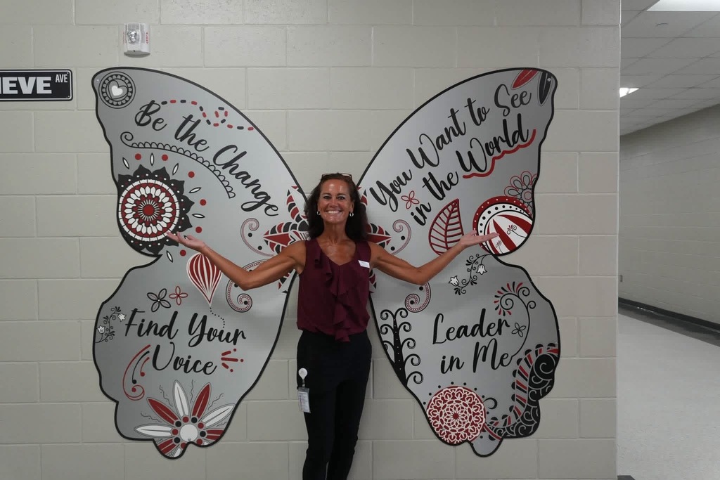 A woman poses next to a large butterfly mural on a wall. The mural has inspirational text.
