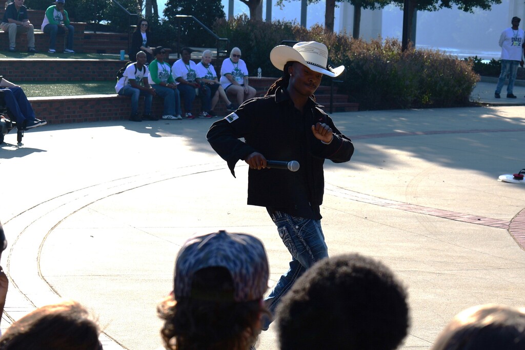 Man in cowboy hat standing in circle performs while a crowd of people watches.