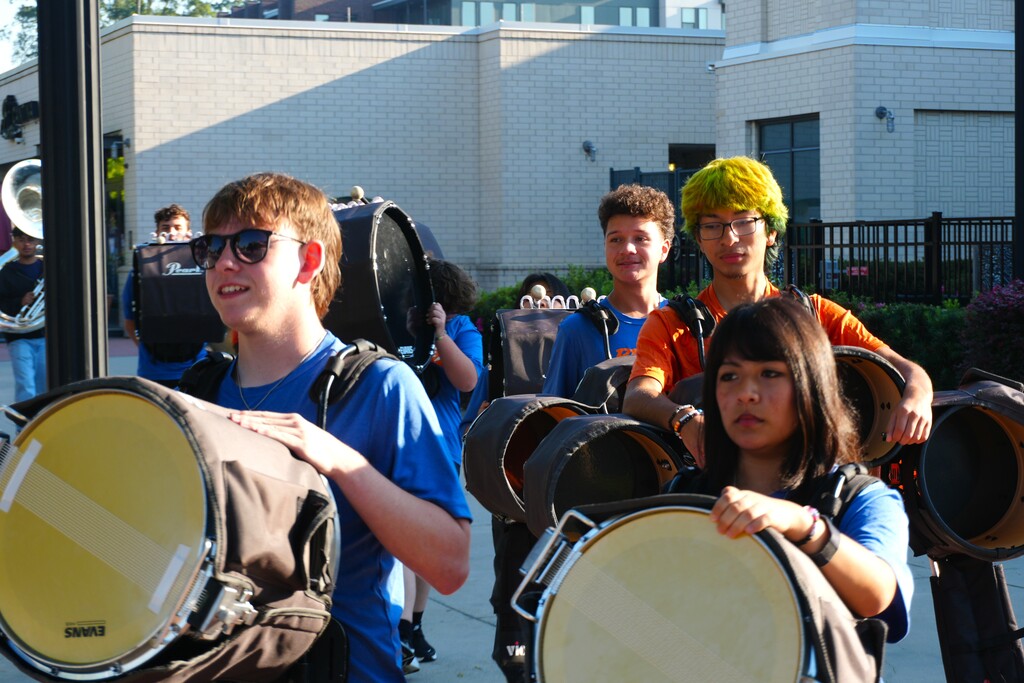 A group of students wearing blue shirts and carrying drums in front of a building.