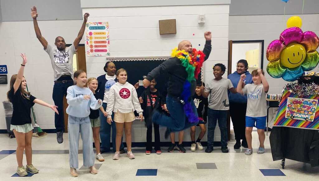 Kids in a room with balloons and decorations; one person jumping in air, others looking up.