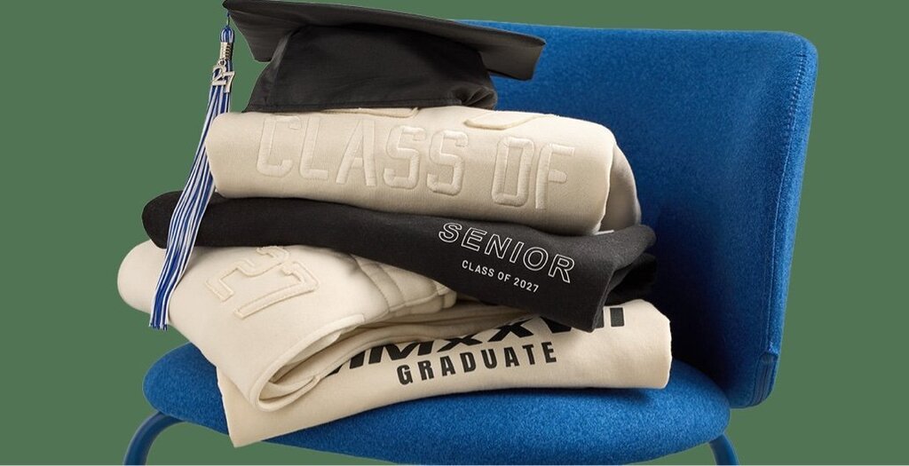Graduation cap and gowns stacked on a blue chair with a green background.